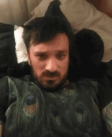 a man with a peacock feather shirt on is laying in bed