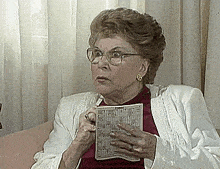 an elderly woman wearing glasses is holding a bingo board