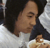 a man in a white shirt is eating a bowl of food with a sign that says ' a ' on it