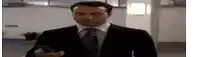 a man in a suit and tie is holding a cell phone in his hand and looking at it .