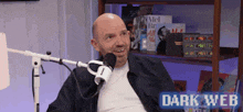 a bald man is sitting in front of a microphone with the words dark web on the bottom .