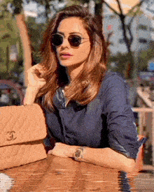 a woman wearing sunglasses sits at a table with a purse