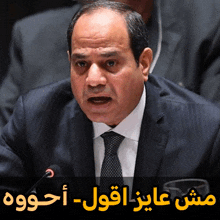 a man in a suit and tie is speaking into a microphone with arabic writing behind him