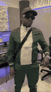 a man wearing a hat and sunglasses stands in front of a computer