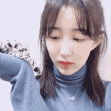 a woman wearing a blue turtleneck sweater and a necklace with a bow on it
