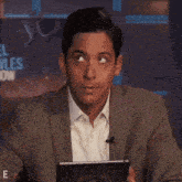 a man in a suit and white shirt is making a funny face in front of a sign that says " el vuelve "