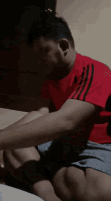 a man in a red shirt with black stripes on the side sits on a bed