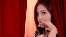 a woman behind a red curtain covering her mouth with her hand