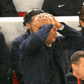 a man in a blue jacket is holding his head with his hands