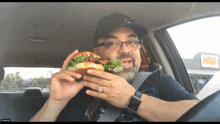 a man is eating a sandwich in a car with a sign that says a&w