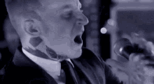 a man with a tattoo on his neck is singing into a microphone while wearing a suit and tie .