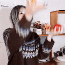a woman in a sweater throws a red apple in front of a shelf that says klasse