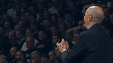a bald man in a suit and white shirt is raising his hands in the air