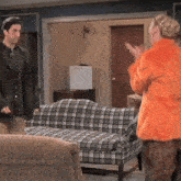 a man and woman are standing in a living room with plaid furniture
