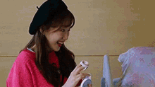a woman wearing a beret and a pink sweater is sitting in a chair holding a bottle .