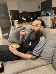 a man with a beard is sitting on a couch with a bowl of popcorn