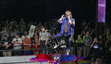 a wrestler is jumping in the air in front of a crowd with a sign that says elp