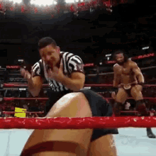 a referee in a striped shirt stands in a wrestling ring with two wrestlers