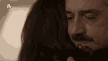 a man with a mustache is hugging a woman with the letters a on the bottom right