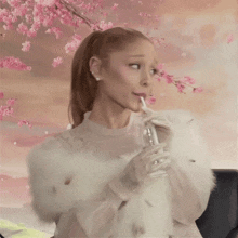 a woman in a white fur coat is drinking from a glass with pink flowers in the background