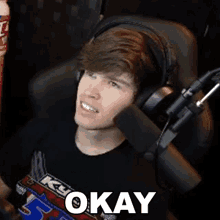 a man wearing headphones is sitting in front of a microphone with the word okay written on it .