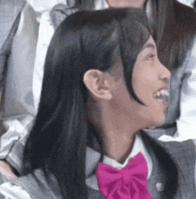 a girl wearing a pink bow tie is smiling while sitting in a chair .