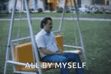 a man is sitting on a swing with the words `` all by myself '' above him .