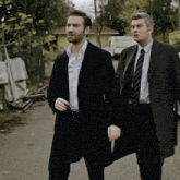 two men in suits and ties are walking down a road