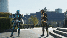 a man in a blue and black costume stands next to another man in a black and orange costume
