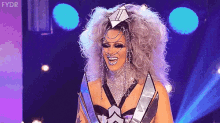 a drag queen is standing on a stage with a trophy and smiling .