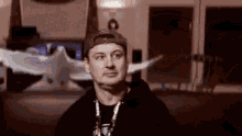 a man wearing a hat and a black hoodie is standing in a dark room .
