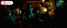two women are sitting in a dark room with a kulfy logo on the bottom right