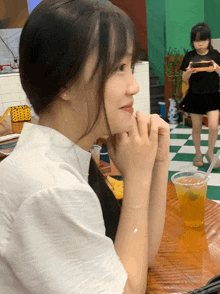 a woman sits at a table with her hands folded in front of a cup of orange liquid