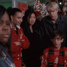 a group of people are standing in front of a christmas tree one of them is wearing a red jacket with the number 2 on it