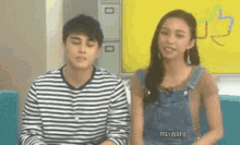 a man and a woman are sitting next to each other on a couch in front of a yellow wall .