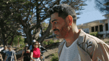 a man with a beard wearing a white shirt and a tan jacket