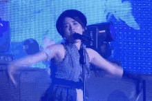 a woman is singing into a microphone on a stage in front of a large screen .