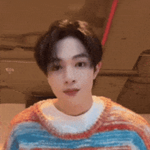 a young man is wearing a colorful sweater and a white shirt .