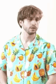 a man with a beard is wearing a hawaiian shirt with pineapples , bananas , and oranges on it .
