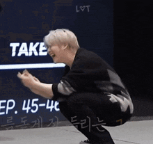a man squatting in front of a wall that says take