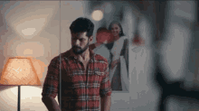 a man in a plaid shirt is standing in front of a mirror with a picture of a woman on the wall behind him .