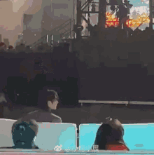 a group of people sitting in front of a stage with chinese writing on the bottom right