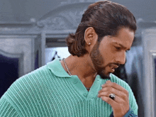 a man with long hair and a beard wearing a green sweater