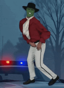 a man wearing a green mask and a red shirt is dancing in front of a police car