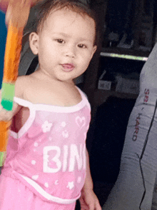 a little girl is wearing a pink tank top that says bin