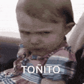 a baby is making a funny face and the word tonito is on the bottom right .