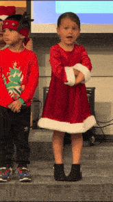 a little girl in a red dress stands next to a boy in a red sweater