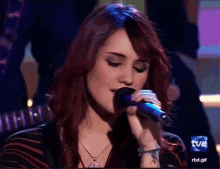 a woman singing into a microphone with the tvb logo in the background
