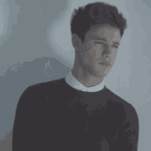 a young man wearing a maroon sweater and white shirt is standing in front of a white wall .