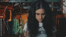 a woman with a tattoo on her arm is wearing a white shirt with a picture of a skull on it
